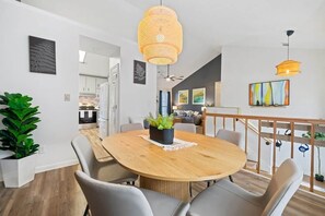 A modern dining area with a round wooden table, grey upholstered chairs, and a hanging wicker light fixture. - Two Homes in One · 5BR/4BA · Theater & Game (Gwinnett County)
