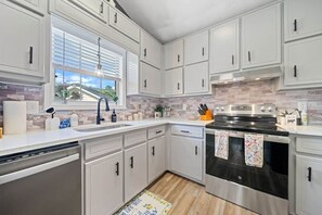 A modern kitchen with white cabinets, a stainless steel oven, and a window with blinds. - Urban CasaOasis 5BR4BA Retreat Theatre & Game (Gwinnett County)