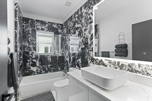 Ein modernes Badezimmer mit Marmorverkleidung, einem großen Spiegel, einer Badewanne, einer Toilette und einem Waschbecken.