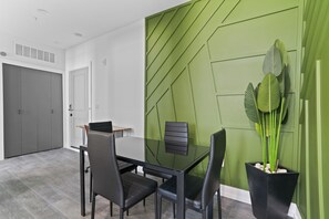 Ein stilvoller Essbereich mit einem Glastisch, schwarzen Stühlen und einer Wand in Grüntönen.