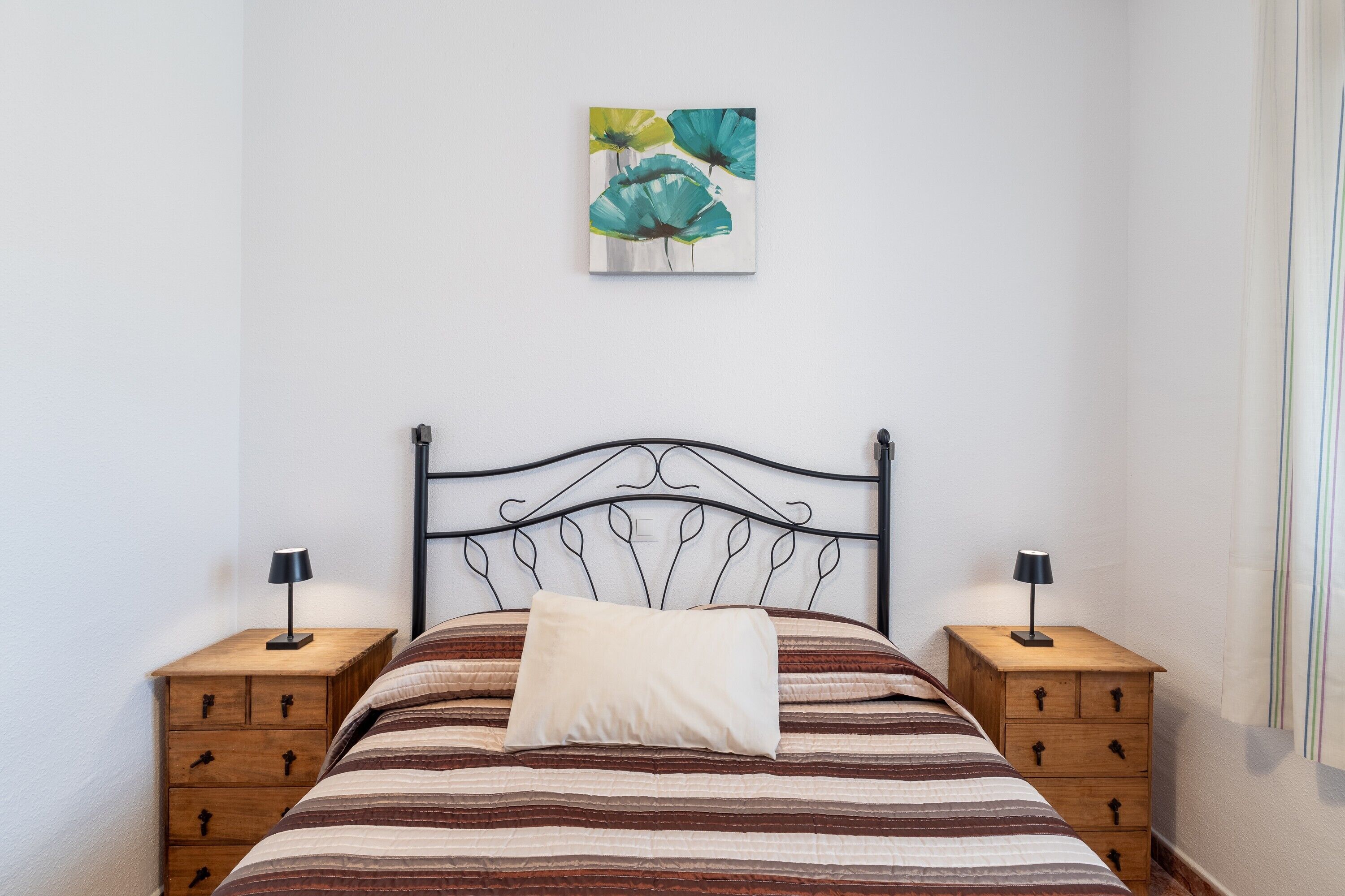 Una cama bien hecha con ropa de cama a rayas, dos mesitas de noche con lámparas y un cuadro colgado en la pared.
