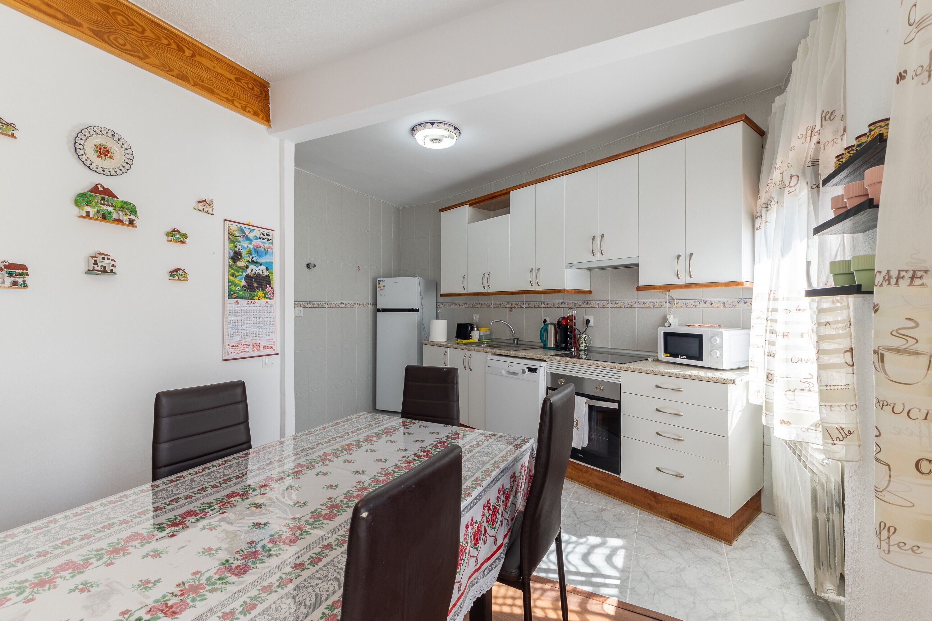 Une cuisine compacte avec des meubles blancs, une table à manger avec des chaises, un réfrigérateur et un four à micro-ondes.