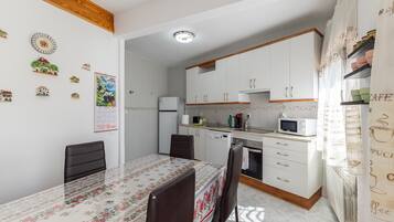 Une cuisine compacte avec des meubles blancs, une table à manger avec des chaises, un réfrigérateur et un four à micro-ondes.