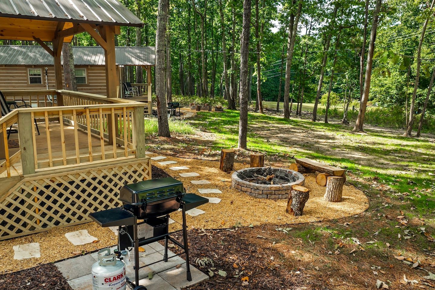 A wooden deck with a grill and propane tank, a fire pit, and a covered seating area.