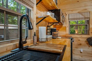 A wooden cabin interior with a kitchen area, including a sink, countertop, and window with a view of trees. - Escape to a Charming Cabin with Hot Tub & Covered Porch in Mentone, Alabama (Mentone)