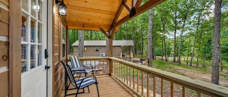 Une terrasse en bois avec un porche couvert, deux chaises et une vue sur un chalet situé dans une zone boisée.
