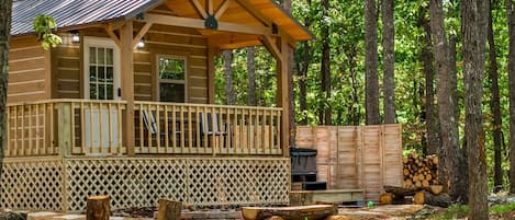A log cabin with a porch, a grill, and stacked firewood.
