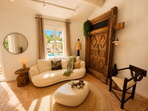 Ein Wohnzimmer mit einer Couch, einem runden Couchtisch, einem Sessel, einem Holzschrank, einem Spiegel und einer Lampe.