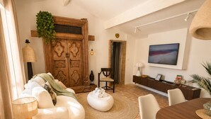 Een ruime woonkamer met een grote houten deur, een bank, een eettafel en een aan de muur bevestigde televisie.