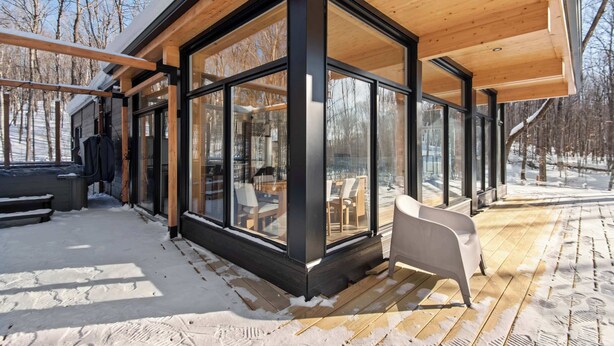 Ein modernes Gebäude mit großen Glasfenstern, einer Holzterrasse und einem Sitzbereich im Freien.