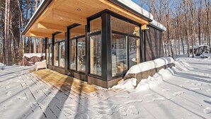Eine moderne Holzhütte mit großen Glasfenstern, einer Holzdiele und verschneitem Gelände.