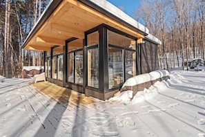 Eine moderne Holzhütte mit großen Glasfenstern, einer Holzdiele und verschneitem Gelände.