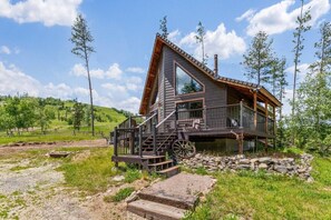 A wooden cabin with a steep roof, a porch, and a stone foundation.