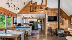 Une cuisine spacieuse de style loft, dotée d’un îlot central, de poutres en bois et d’une grande fenêtre donnant sur un espace verdoyant.