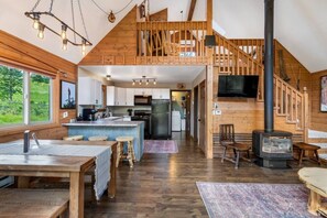 A spacious loft-style kitchen with a central island, wooden beams, and a large window overlooking greenery.