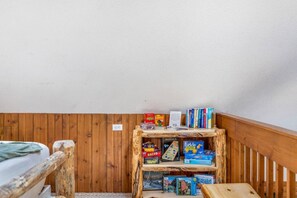 A small room with wooden walls and a sloped ceiling. There is a wooden shelf with various board games and books. - Elk Pointe Chalet- Hot Tub and Views! (Lead)