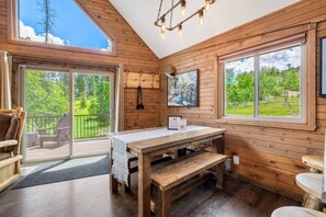 A wooden cabin interior with a table, bench, and two chairs.