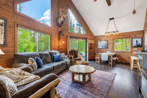 A log cabin interior with a sofa, chairs, a dining table, and a kitchen area.
