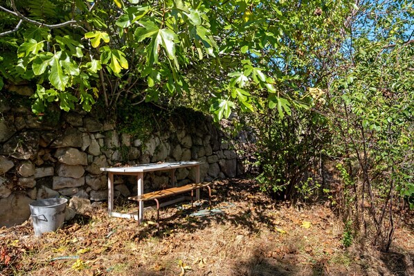 A stone wall with a metal table and bench, surrounded by greenery and a clear sky.