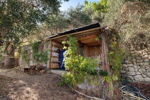 A rustic outdoor structure with a wooden roof, surrounded by vegetation and a stone wall. - La Petite Bergerie in the Meadow – Authenticity, Nature & Panoramic Views (Coaraze)