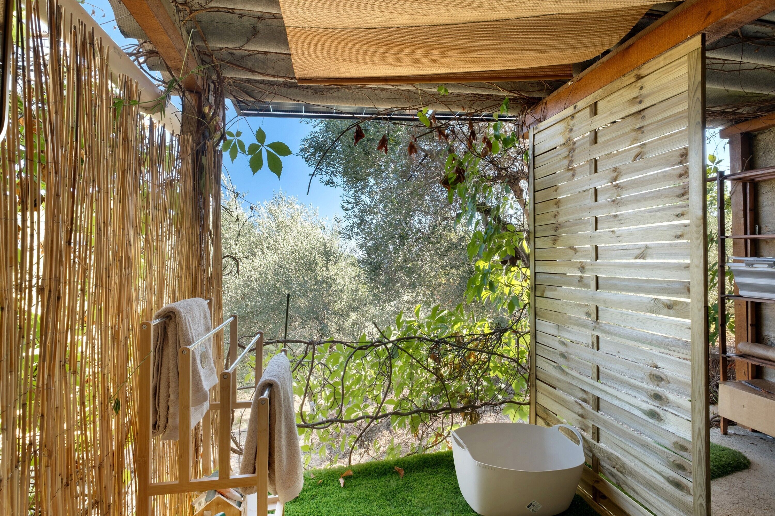 Un espace extérieur aménagé avec des sièges en bois, une clôture en bambou, un bac en plastique blanc et un porte-serviettes.