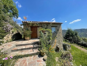A stone house with a wooden door, steps leading to the entrance, and a satellite dish on the roof.