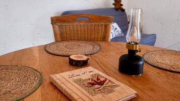 Une table ronde en bois, sur laquelle repose un set de table tissé, un petit sous-verre en bois, un porte-bougie en verre et un livre intitulé « Livre L’Ore ».
