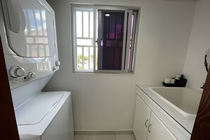 Ein kleines Badezimmer mit Waschmaschine, Badewanne und einem fensterbelaubten Fenster.
