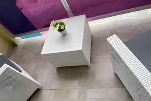 Ein weißer Tisch mit einer kleinen Pflanze, ein Kachelboden und eine violette Wand im Hintergrund.