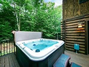 Ein Whirlpool auf einer Terrasse mit Holzhütte im Hintergrund.