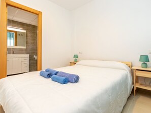 Ein Hotelzimmer mit einem Bett, einem Nachttisch aus Holz mit einer Lampe, einem Badezimmer mit Spiegel und Waschbecken sowie einem Handtuchhalter mit Handtüchern.