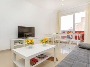 Un salon moderne doté d’un téléviseur  à écran plat, de meubles blancs, de deux vases et d’un balcon aménagé avec un coin repas.
