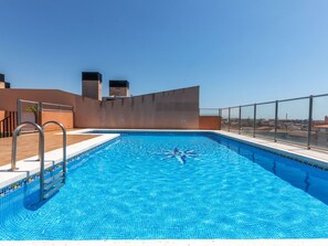 Ein Pool auf dem Dach mit klarem, blauem Wasser, Metallgeländern und Blick auf die Stadt.