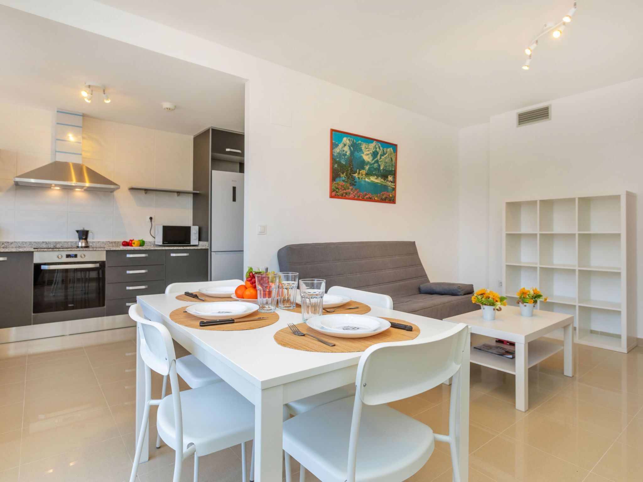 Une cuisine moderne avec un coin repas, un canapé gris et un tableau au mur.