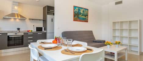 A modern kitchen with a dining area, a gray sofa, and a painting on the wall.