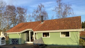 A green house with a tiled roof, a chimney, and a covered outdoor seating area. - 4 Star Holiday Home in Stubbekobing (Stubbekobing)