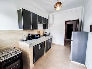 A modern kitchen with black cabinets, a gas stove, a coffee machine, and a refrigerator. - L'Escale piscine et cinéma (Abidjan)