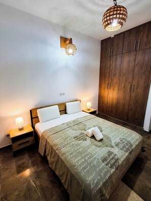A bedroom with a bed, bedside lamps, a wooden wardrobe, and a hanging light fixture. - L'Escale piscine et cinéma (Abidjan)