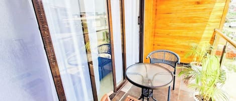 Un balcon avec une porte-fenêtre, une table ronde, deux chaises et un pot de fleurs.
