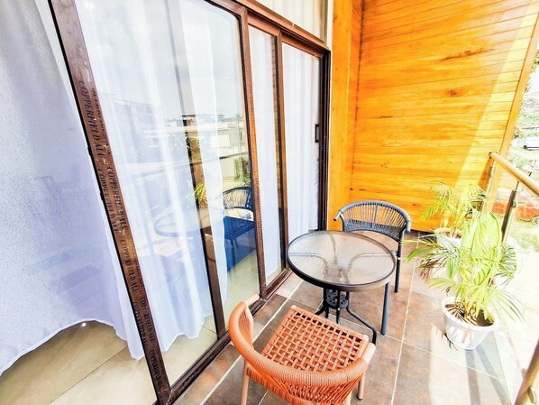 A balcony with a glass door, a round table, two chairs, and a potted plant.