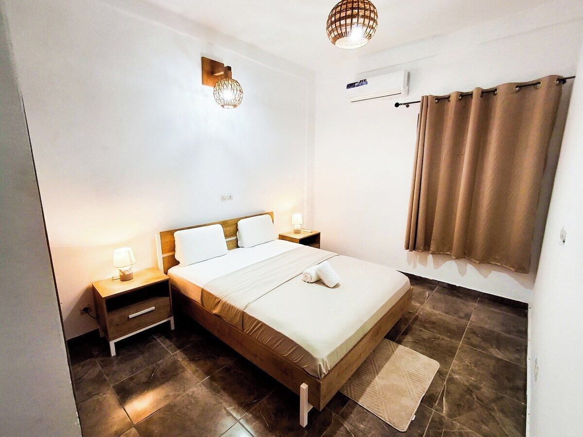 Een slaapkamer met een bed, nachtkastjes, een wandairconditioner en een gordijn.