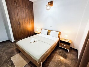 A bedroom with a bed, wooden wardrobe, bedside tables with lamps, and a wall-mounted light fixture.