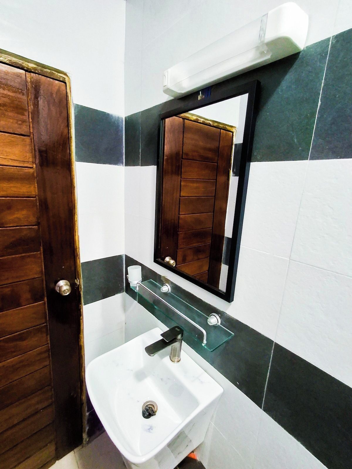 A bathroom with a wooden door, a white sink, a glass shelf, and a mirror.