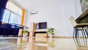 Et moderne hotelværelse med et stort fladskærms-tv, et træskab, et glastbord og to krukkeplanter.
