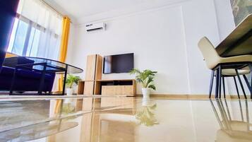 Een moderne hotelkamer met een grote flatscreen-tv, een houten kastje, een glazen tafel en twee potplanten.