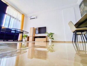 Een moderne hotelkamer met een grote flatscreen-tv, een houten kastje, een glazen tafel en twee potplanten.