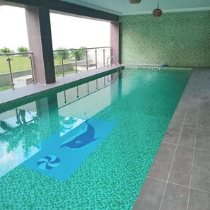 An indoor swimming pool with clear water, a lifeguard stand, and a view of the outdoors.