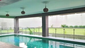 Indendørs swimmingpool med glasvægge, et metalgelænder og udsigt til en græsplæne.