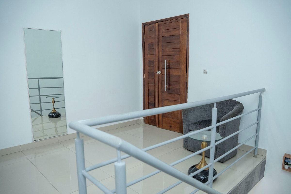 A room with a wooden door, a glass table with a gold base, and a grey armchair.