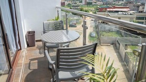Ein Balkon mit Tisch und Stühlen, einer Glasreling und Blick auf eine Stadtansicht.